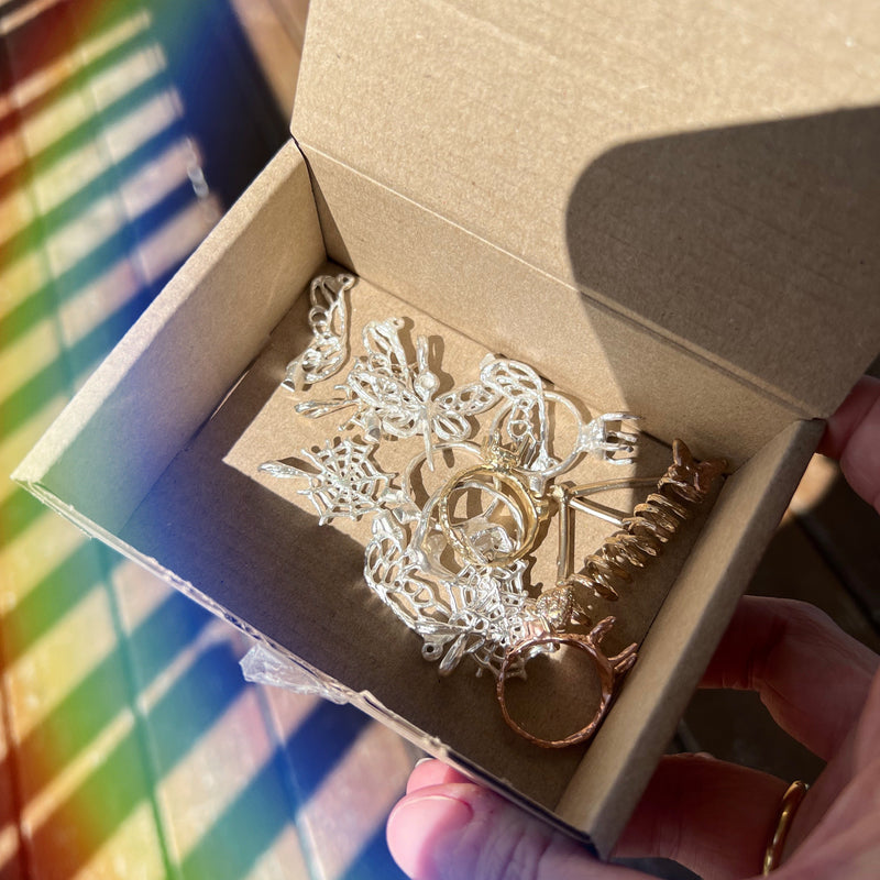 Gold and silver keychain in a cardboard box held by a hand with a rainbow background