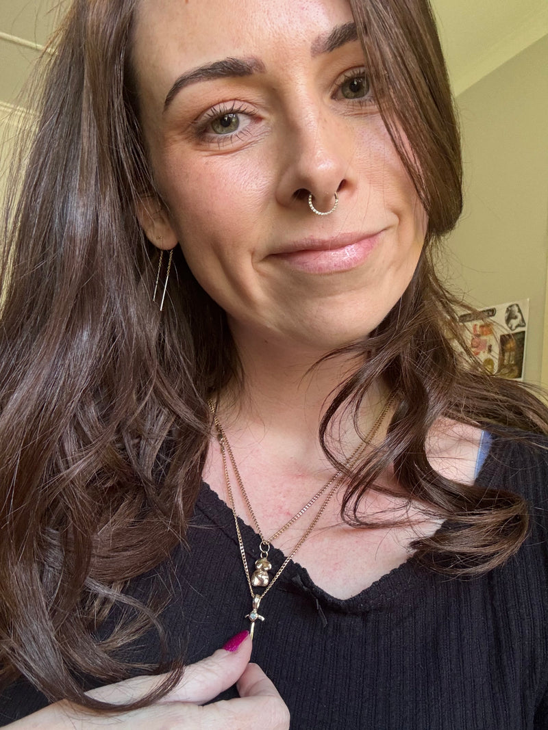 Close-up of a person with long brown hair and a nose ring, wearing a dark top.