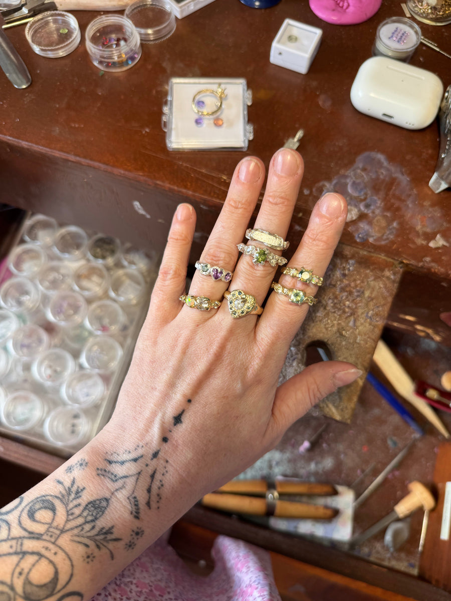 Hand wearing multiple rings on a jewelry-making table with tools and materials.