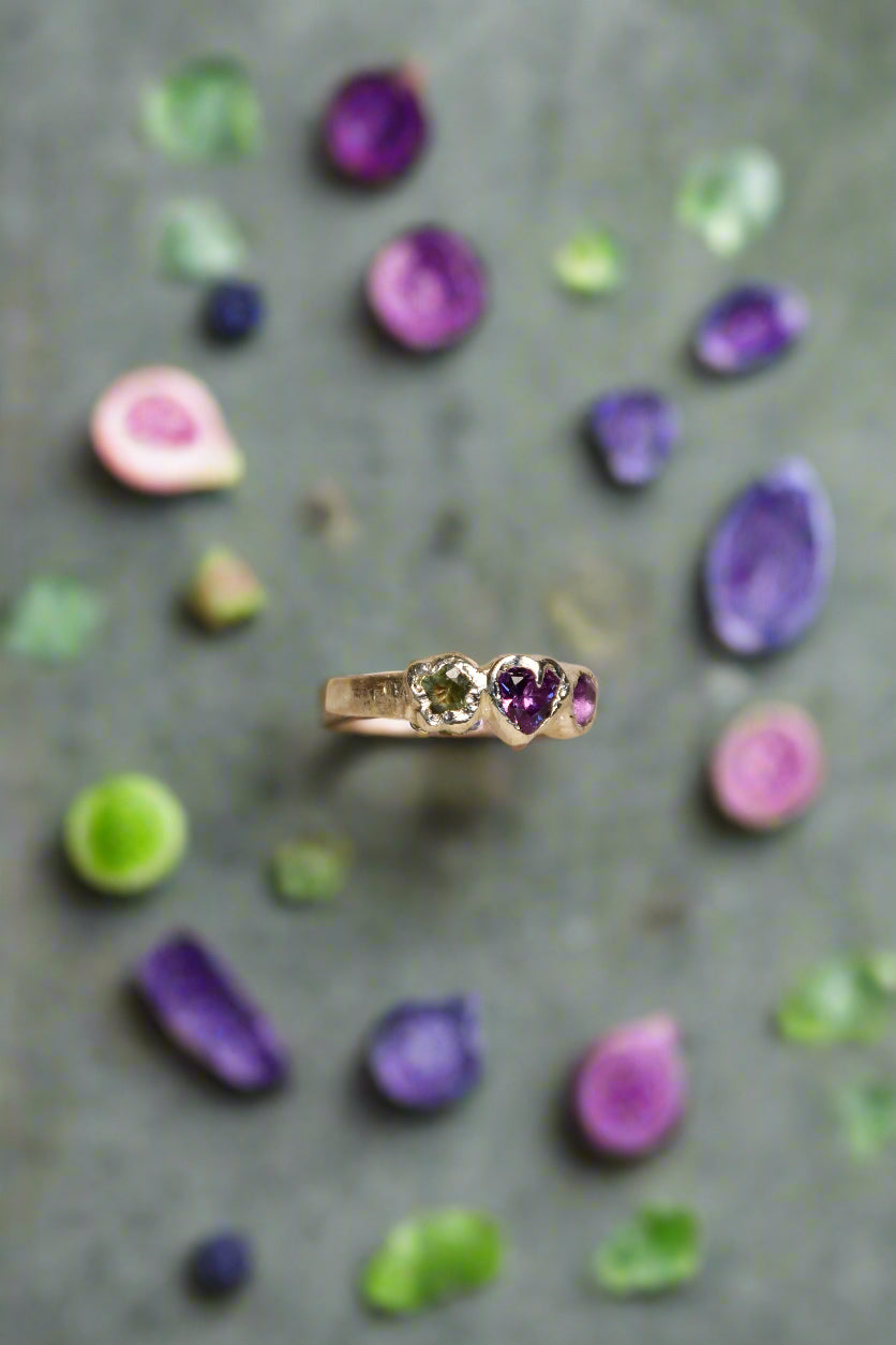 Silver ring with green and purple gemstones on a beige background