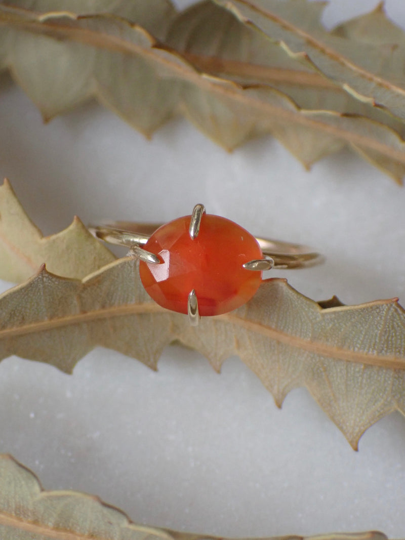 Four Prong Carnelian Ring Made of Gold on white background with leaves 