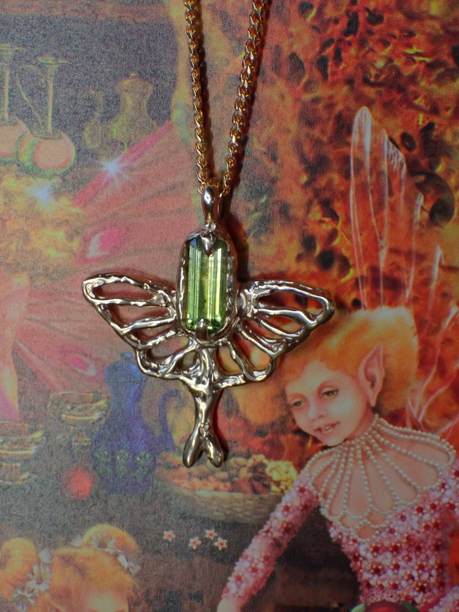 Luna Moth pendant with green peridot and golden wings, on chunky curb chain in front of fairy book